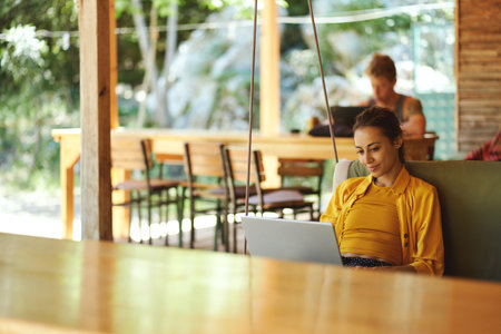 Pretty woman checking her mail on portable laptop in summer cafe shop or coworking hub. Summer vacations and sometimes working remotelyの写真素材