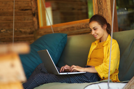 Young business woman working remote on laptop computer on business projects while sitting on swing in cafeの写真素材