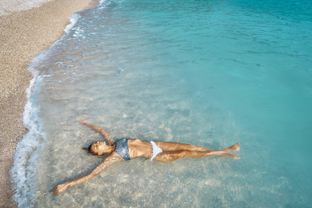Sexy suntan perfect skin bikini woman relaxing on beach, lying in shallow water in turquoise mediterranean sea in Oludeniz Beach in Aegean Seaの写真素材