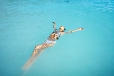 Perfect body woman in swimsuit bikini relaxing in blue ocean water, enjoying her summer vacation, feeling happiness and carefreeの写真素材
