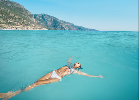 High angle view of beautiful vacation woman relaxing in the sea. Carefree girlin bikini floating in transparent turquoise waterの写真素材