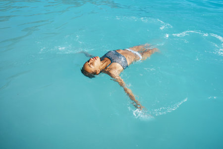 Sensual relaxed woman floating on her back in the ocean. Tanned lady sunbathing, enjoying summer vacation in clear blue waterの写真素材