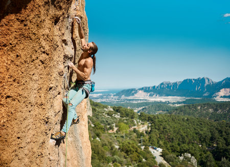 Strong muscular body man rock climber climbing on height vertical rock with rope on a mountains and blue sky background. Outdoor sports and recreationの写真素材
