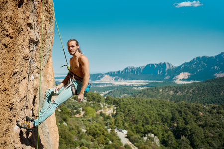 Handsome sporty man rock climber hanging on rope and looking to camera. Muscular male resting before climbing on difficult routeの写真素材