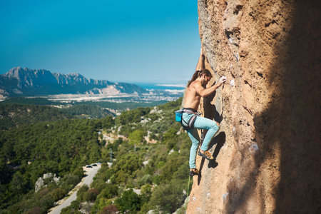 Beautiful strong male climbing on height vertical cliff with rope on a mountains and blue sky background. Outdoor sports and recreationの写真素材