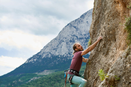Active young man rock climber gripping hold, working on challenging route on cliff, beautiful mountains view on backgroundの写真素材