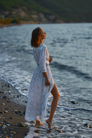 Beautiful young romantic woman in elegant boho white dress outdoors at twilight or evening time on the beachの写真素材