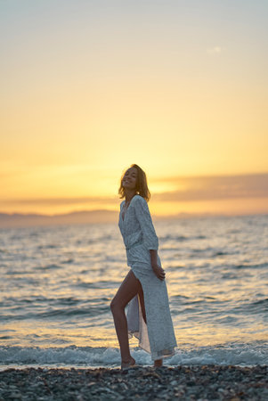 Attractive young elegant lady in dress enjoying sunset time at the beach. Background orange sundown on the seaの写真素材