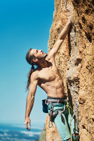 Vertical portrait handsome muscular man climber looking up with tense face and gripping hold. Rock climbing and active lifestyle conceptの写真素材