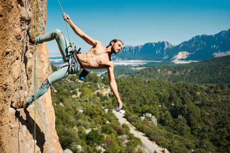 Fit body handsome man rock climber looking away on height vertical rock with rope. Amazing nature view on backgroundの写真素材