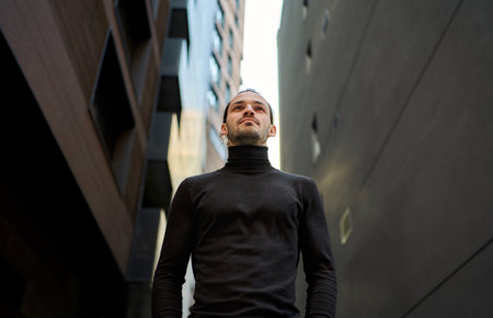 Confident ambitious man standing between two tall buildings with skyline, looking ahead with determination and purpose. Concept of strength, confidence, and the power of choiceの写真素材