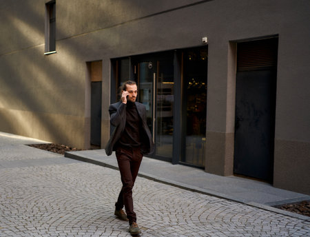 Urrban Image of confident young businessman in black suit walking on the street while busy talking on the phone call. Perfect for commercial projects related to business and electronics.の写真素材