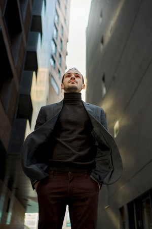 Confident man in black suit standing between two tall buildings with skyline, looking ahead with determination and purpose. Concept of strength, confidence, and the power of choiceの写真素材
