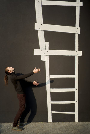 Man in black wear standing sideways with his arms stretched out to illustrated staircase going upwards. The ladder is a visual representation of the social hierarchy. Ascending to Social Ladderの写真素材