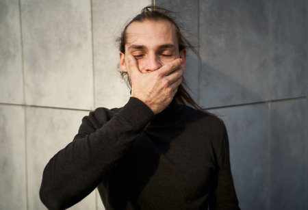Close up portrait of young man covering his mouth by hands, symbolizes the silence and suppression of important issues that need to be addressedの写真素材