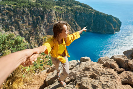 Happy tourist woman holding her boyfriend hand, showing him towards the breathtaking scenery of Butterfly Valley Beach. Couple exploring scenic landscape with crystal clear turquoise waterの写真素材