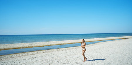 Beautiful panoramic image of idyllic coastal getaway. Suntan woman walking almong serene secluded sandy beach with seaviewの写真素材