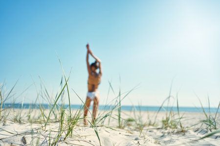 Serenity image of a stunning sunny beach. On background unfocused back view of woman reaching her arms up towards blue sky on white sandy seashoreの写真素材