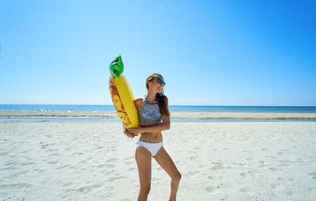 Happy beach woman holding inflatable pineapple float ring against coastal backdrop. The vibrant colors, playful atmosphere at seashoreの写真素材