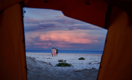 View from camping tent on three friends walking on serenity peaceful beach with purple sky at sunsetの写真素材