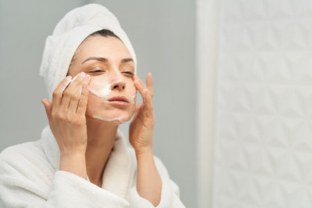 Close up skincare routine portrait of female. Adult woman wearing towel on head massaging face with foam for face washingの写真素材