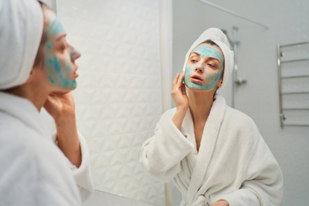 Stunning lady standing at bathroom and applying a natural skin-nourishing facial mask. Beauty of home skincare rituals and feel rejuvenatedの写真素材