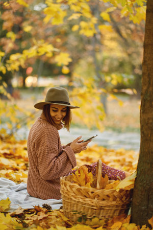 Beauty of autumn in this atmospheric image. Young fashionable woman enjoying picnic amidst the...