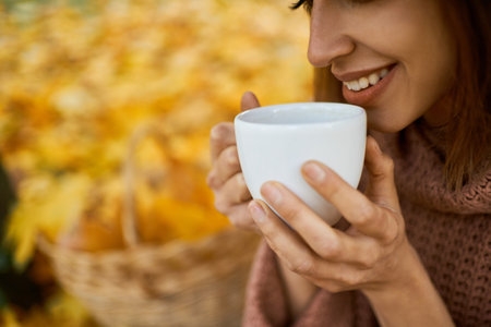 Close up lips of woman drinking hot coffee, holding white cup in hands at autumn parkの写真素材