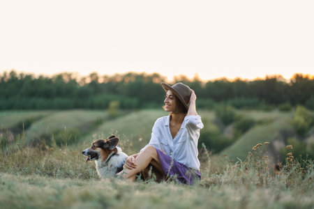 Young lady and her pet Corgi dog spending quality time in nature, overlooking scenic with grassy hillsの写真素材