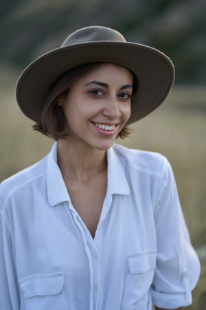 Portrait of beautiful stylish woman with a hat looking to camera in field with dry yellow grass.の写真素材