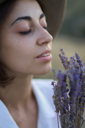 Close up face of beautiful young woman in hat enjoying the aroma of lavender flowersの写真素材