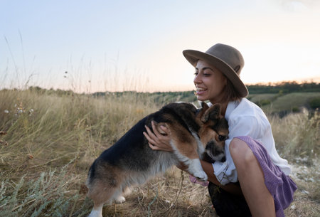 Adorable funny Welsh Corgi dog joyfully jumping onto its owner woman amidst a vibrant field.の写真素材