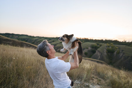 Happy man holds his fluffy Welsh Corgi dog outdoors. Cute fluffy pet and its owner sharing a special moment togetherの写真素材