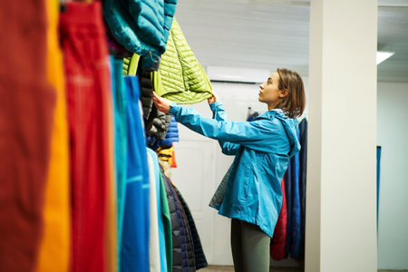 Stylish young woman selecting a jacket in a trendy clothing store. Concept of consumerism, shopping, fashion choices, retail therapy, and lifestyle conceptsの写真素材