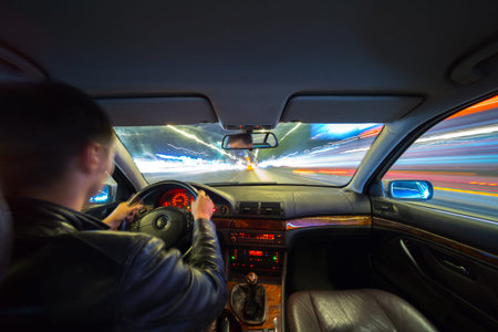 Driver in a car moves at fast speed at the autum night. Blured road with lights with car on high...
