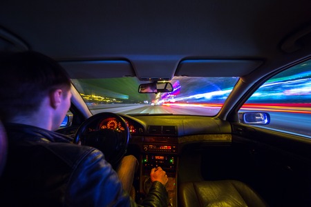 Driver in a car moves at fast speed at the autum night. Blured road with lights with car on high speed.の写真素材