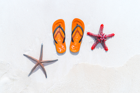 Orange flip flops and two starfish on white sandy beach. Summer vacation conceptの写真素材
