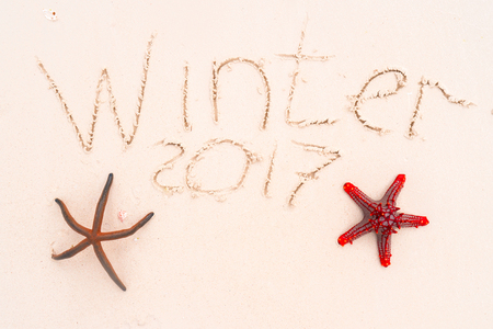 The inscription winter 2017 and two starfish on white sandy beach. Summer vacation conceptの写真素材