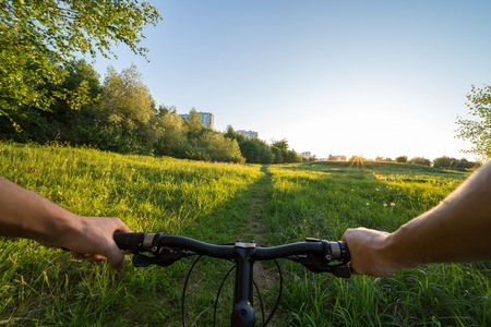 Hands holding handlebar of a bicycle with green meadow on background. View from bikers eyes.の写真素材