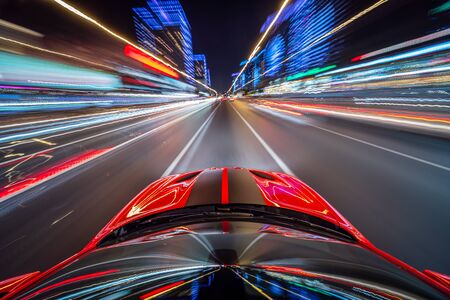 View from roof of the red muscle car Car moving in a night city, Blured road with lights with car on high speed. Concept rapid rhythm of a modern city.の写真素材