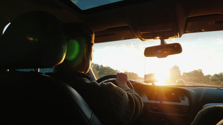 An Asian man drives a car along the highway, the setting sun shines in the windshield. Back viewの写真素材