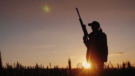 Silhouette of a woman with a gun in her hands. Hunter in the field at sunsetの写真素材