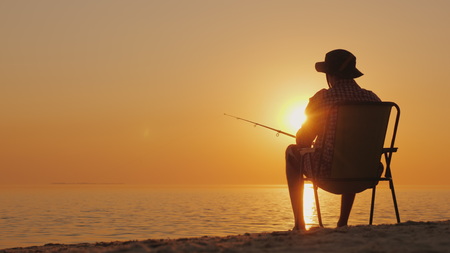 A young man is sitting on the seashore, fishing. Relaxing in the open air.の写真素材