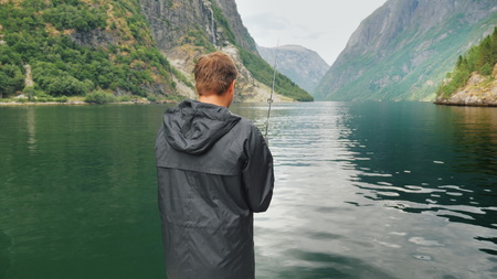 The man is fishing on the background of the mountains in the picturesque fjord of Norway. Fishing in Norway conceptの写真素材
