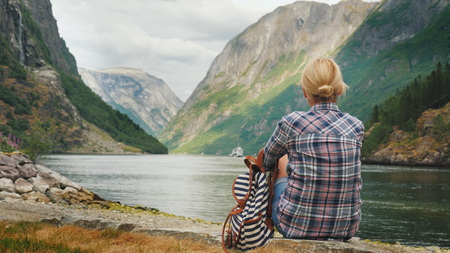 A woman sits on the shore of a picturesque fjord in Norway, admires the beautiful view of the Neroy-fjord, a branch of the Sognefjord. Tourism in Scandinaviaの写真素材