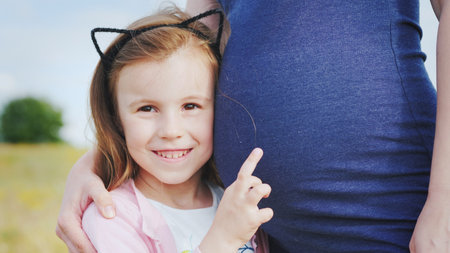 Portrait of a cute girl near the belly of her pregnant motherの写真素材