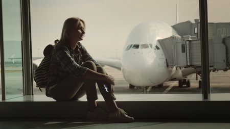 A single woman is sitting on the windowsill in the airport terminal amid a huge airliner. Loneliness and parting conceptの写真素材