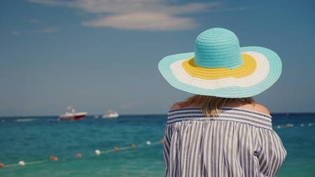 A woman in a hat admires the sea, a rear view. Woman on vacation conceptの写真素材