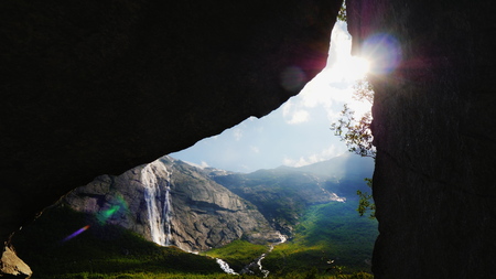 The sun shines through the arch in the rock, where you can see the picturesque valley surrounded by high mountains. The amazing nature of Norway, the tourists dreamの写真素材