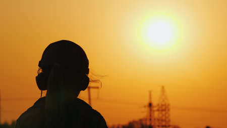 Girl in headphones listening to the radio on the background of the cityscape and beautiful orange...